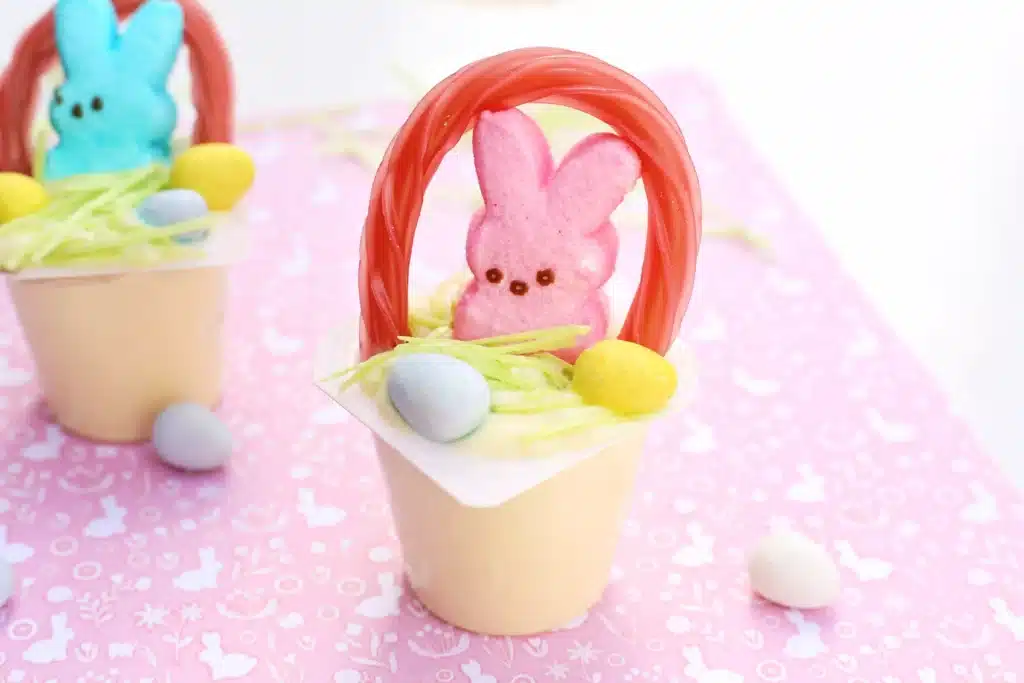 Easter Basket Pudding Cups - Cultivating Brilliant Minds a vanilla pudding cup with edible grass, cadbury mini eggs, a peep, and a twizzler bent to look like a handle