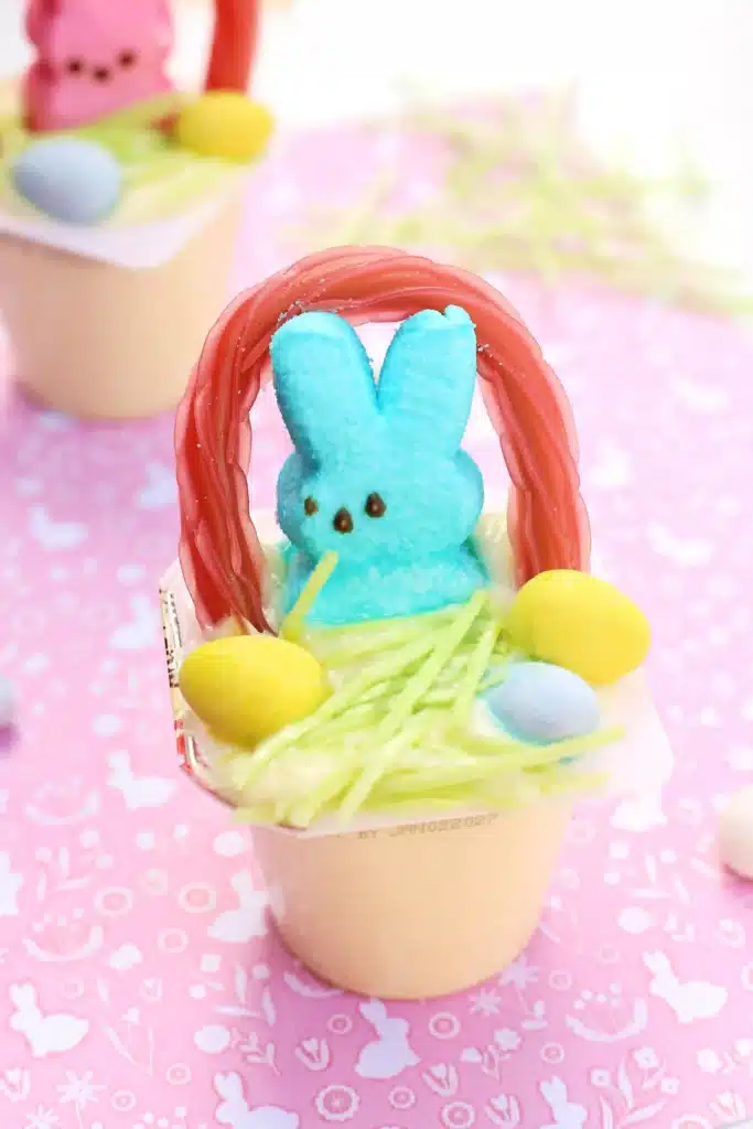 Easter Basket Pudding Cups - Cultivating Brilliant Minds a vanilla pudding cup with edible grass, cadbury mini eggs, a peep, and a twizzler bent to look like a handle