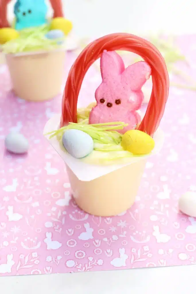 Easter Basket Pudding Cups - Cultivating Brilliant Minds a vanilla pudding cup with edible grass, cadbury mini eggs, a peep, and a twizzler bent to look like a handle
