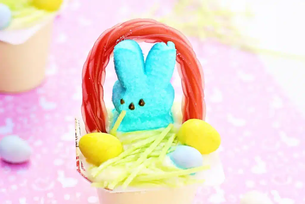 Easter Basket Pudding Cups - Cultivating Brilliant Minds a vanilla pudding cup with edible grass, cadbury mini eggs, a peep, and a twizzler bent to look like a handle
