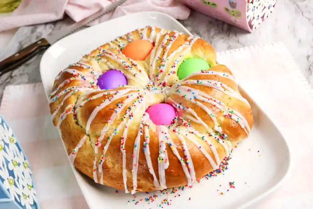 Italian Easter Bread Recipe - Cultivating Brilliant Minds a braided italian easter bread with colored eggs, glaze, and sprinkles