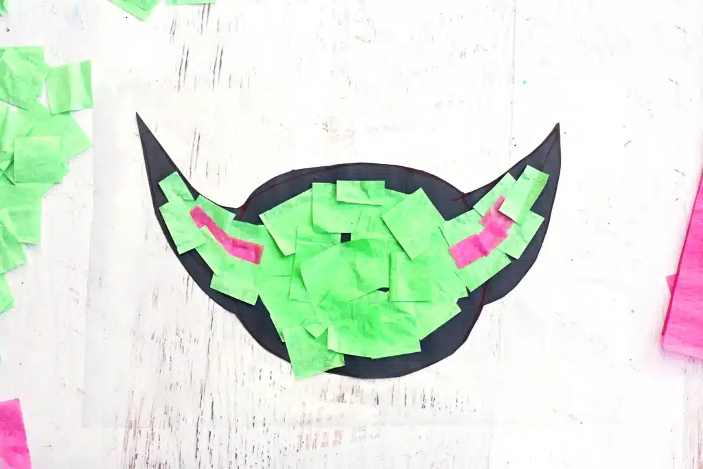 Fill entire silhouette with tissue paper - Cultivating Brilliant Minds contact paper with a black construction paper outline of baby yoda and green and pink tissue paper