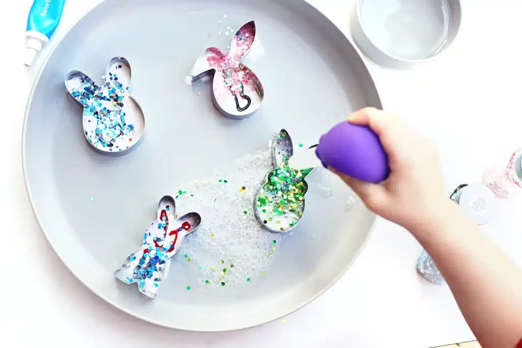 Fizzy Bunny Experiment - Cultivating Brilliant Minds a kid dropping vinegar into a cookie cutter filled with baking soda, food coloring, and glitter