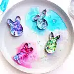 Fizzy Bunny Experiment - Cultivating Brilliant Minds cookie cutters on a plate with baking soda, glitter, food coloring, and vinegar