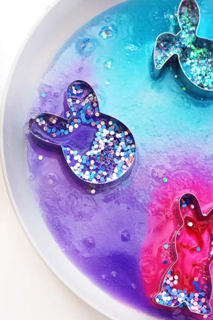 Fizzy Bunny Experiment - Cultivating Brilliant Minds cookie cutters on a plate with baking soda, glitter, food coloring, and vinegar in it to create a "volcano"