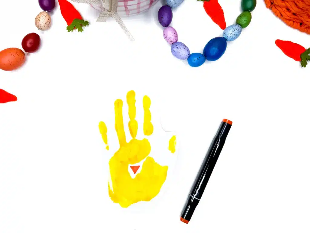 Chick Handprint Craft - Cultivating Brilliant Minds a yellow paint handprint on a piece of paper with an orange beak drawn on in marker to create a spring craft of a chick