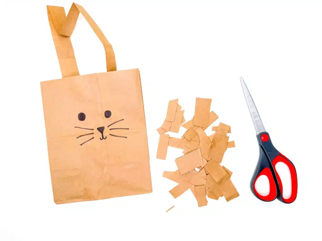 Paper Bag Bunny Basket Craft - Cultivating Brilliant Minds a paper bag decorated to look like a bunny next to strips of paper bag