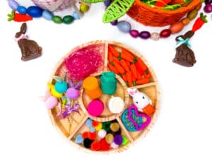 an easter playdough tray with playdough, cookie cutters, easter grass, pom poms, and mini carrots