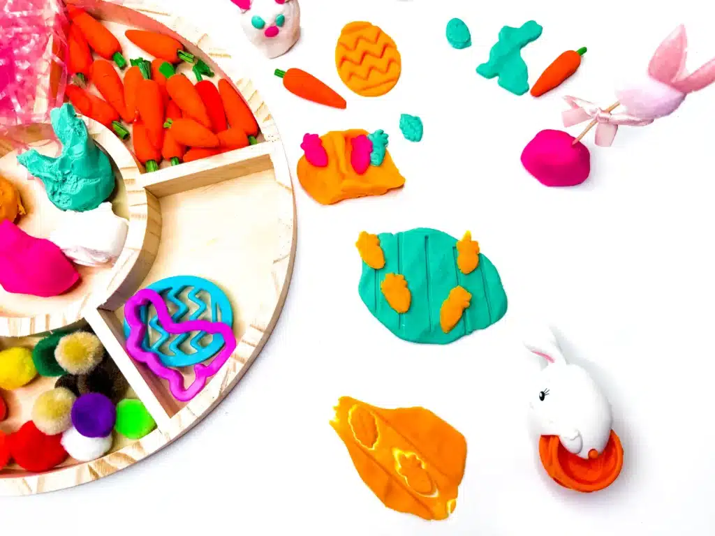 an easter playdough tray with playdough, cookie cutters, easter grass, and mini carrots