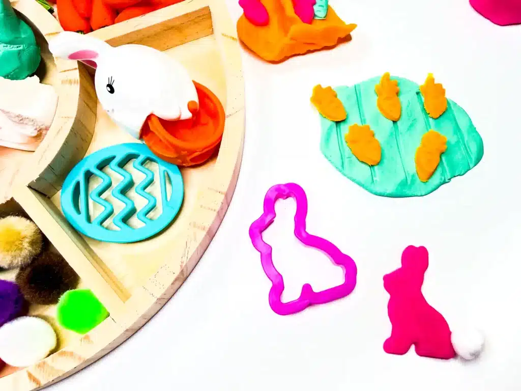 a bunny cut out of playdough with a pom pom and carrots cut out of orange playdough for an easter activity with playdough