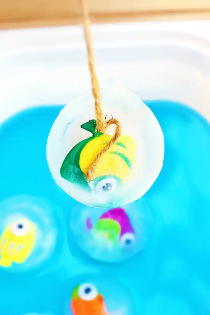 Ice Fishing Sensory Bin - Cultivating Brilliant Minds a kid picking up a fish frozen in ice with twine