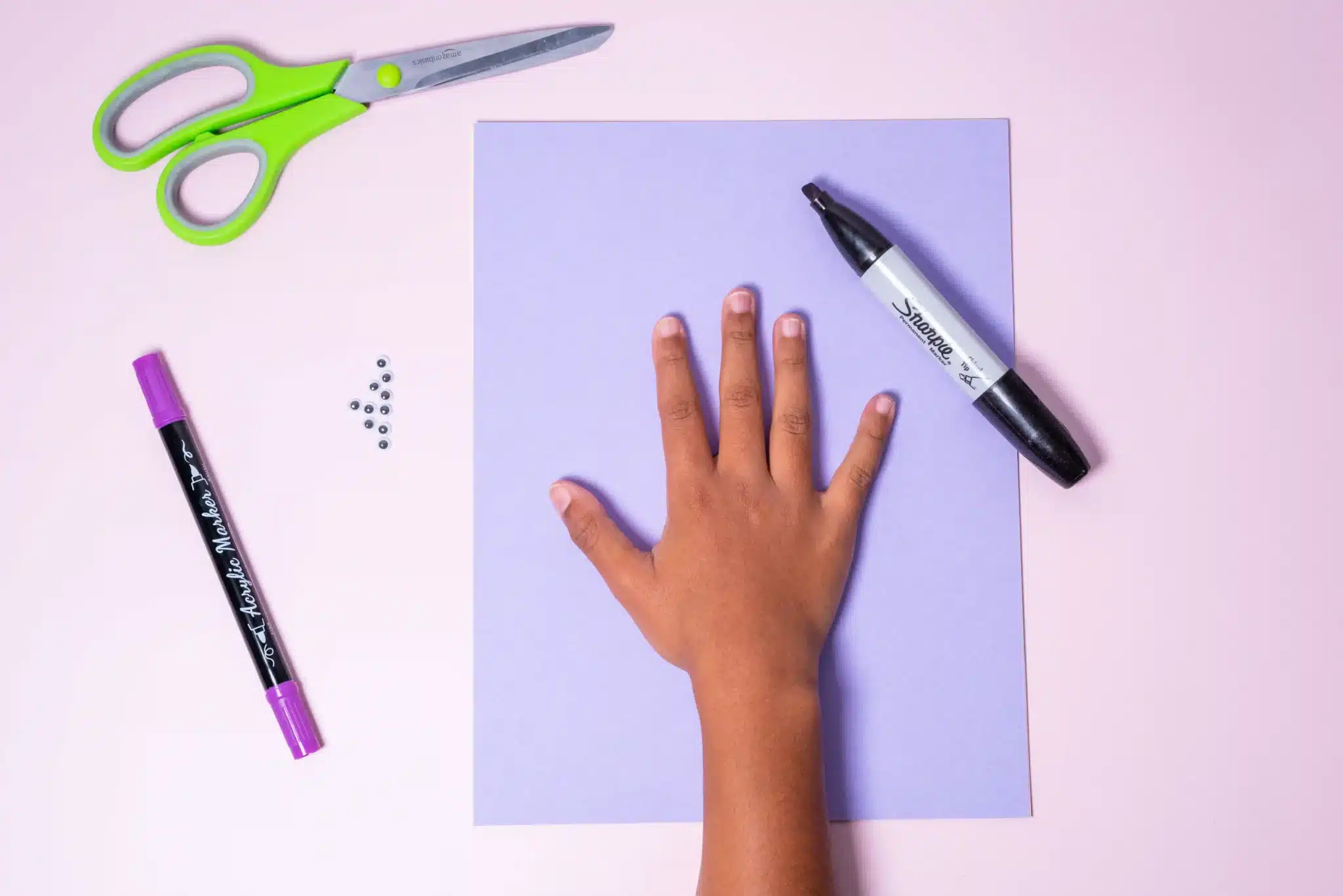 Bunny Handprint Craft - Cultivating Brilliant Minds a kid's hand on top of purple paper with a sharpie next to it
