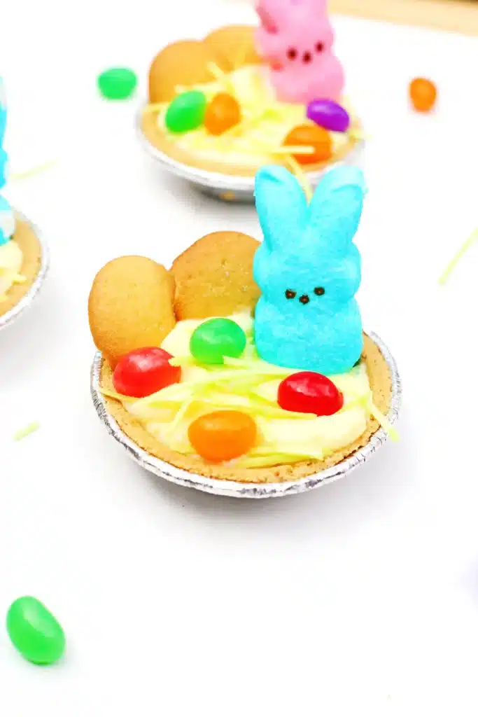 Peeps Banana Pudding Mini Pies - Cultivating Brilliant Minds a banana pudding mini pie with nilla wafers, edible grass, jelly beans, and a peeps bunny