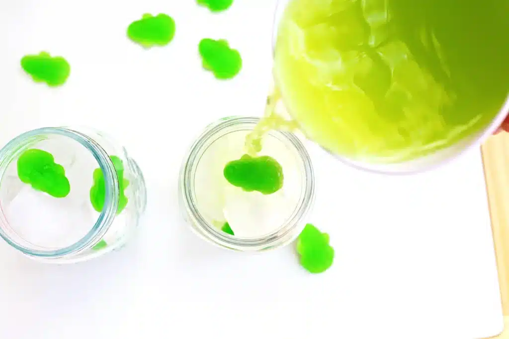 Frog Pond Punch - Cultivating Brilliant Minds pouring a pitcher of juice into a mason jar with ice and frog gummies