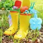 Rain boots Easter basket for kids - Cultivating Brilliant Minds rain boots with easter grass, seed bomb eggs, and toy garden tools inside and a spray bottle handing