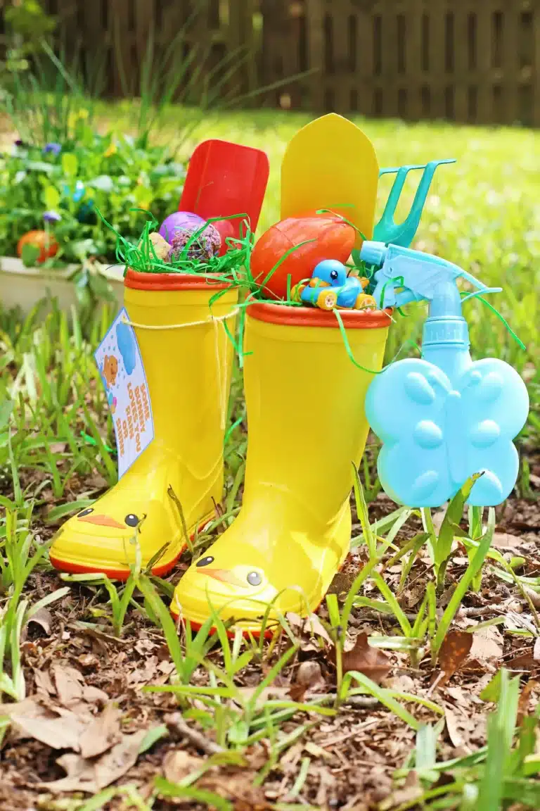 rain boots with easter grass, seed bomb eggs, and toy garden tools inside and a spray bottle handing