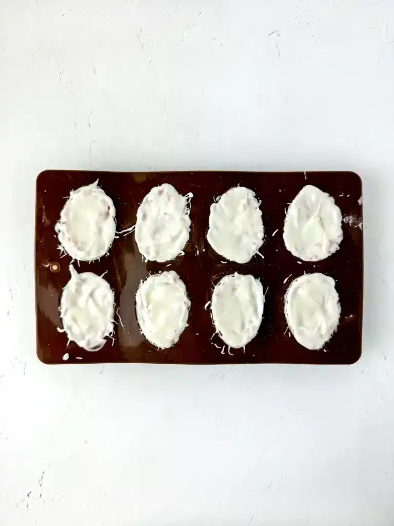 a mold shaped like eggs with white chocolate and a strawberry cupcake mixture inside