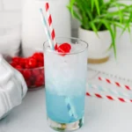 Copycat Sonic Ocean Water - Cultivating Brilliant Minds Tall glass of icy blue beverage with red cherries, two striped straws, and a blurred kitchen scene in the background.