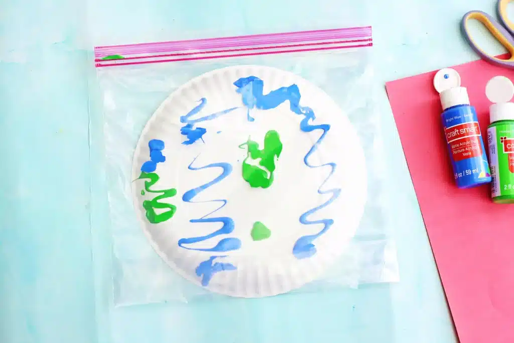 No-Mess Earth Day Painting - Cultivating Brilliant Minds green and blue paint on a paper plate inside a plastic bag