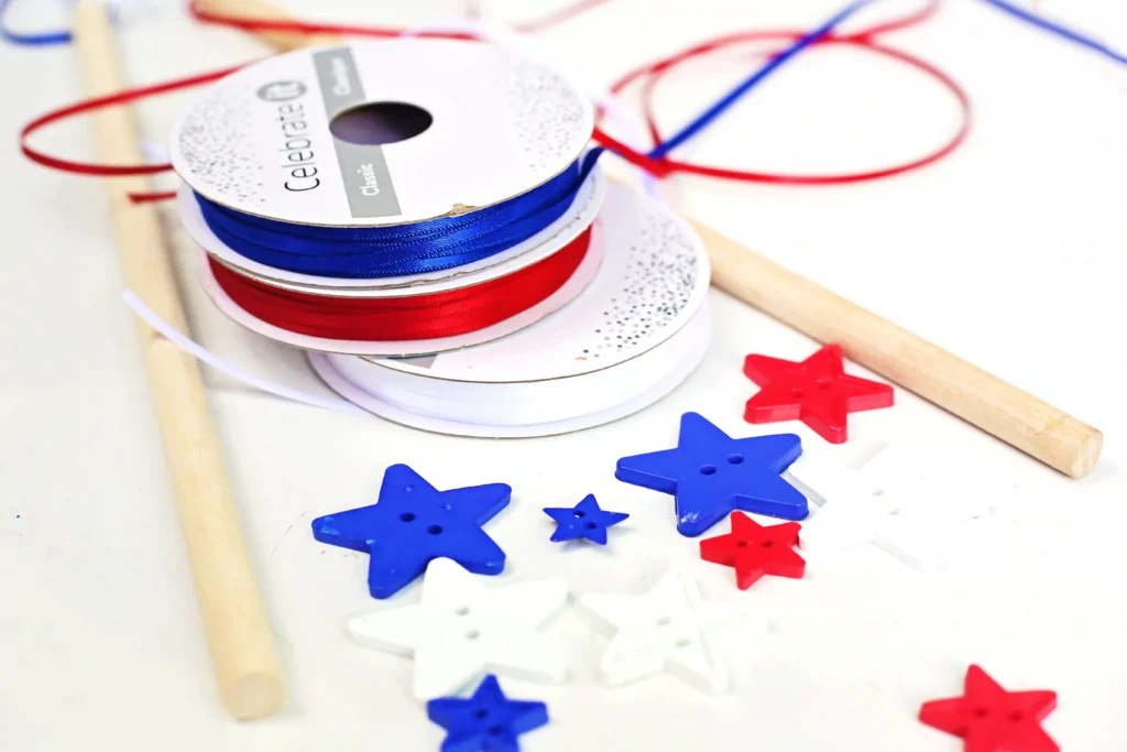 American Flag Wands - Cultivating Brilliant Minds Close-up of blue and red ribbon spools with star-shaped confetti scattered on a white surface and wooden sticks nearby.