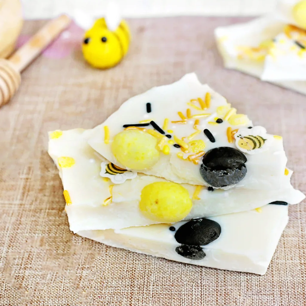 Bee-themed cookies with yellow and black decorations on a light wooden surface, plus a small bee figurine nearby.