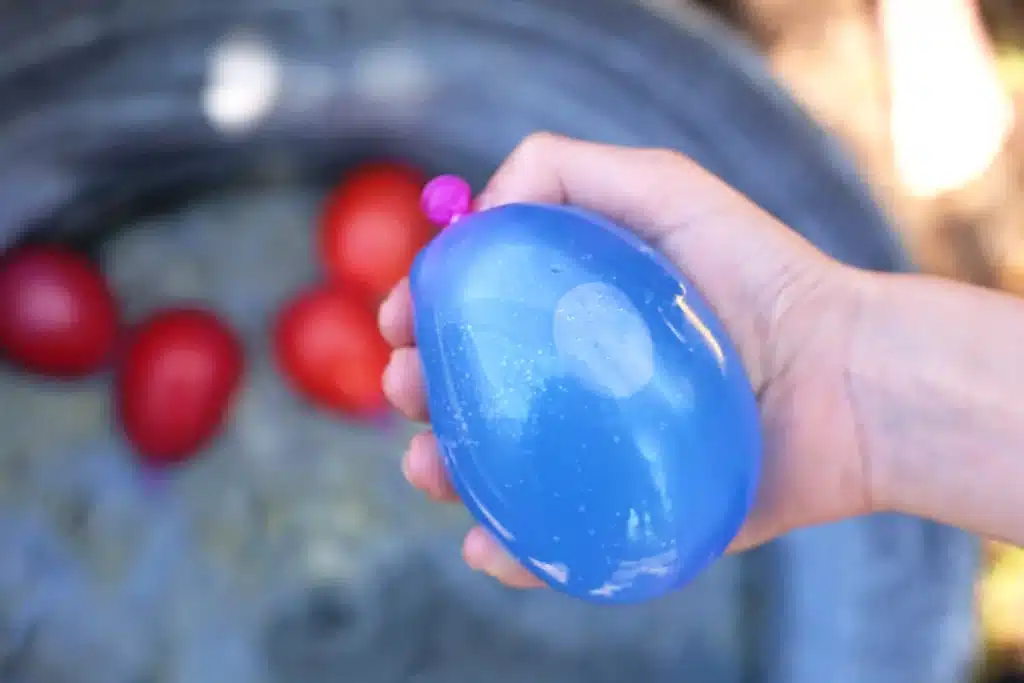 Water Balloon Splatter Art - Cultivating Brilliant Minds Person holding a blue water balloon with red balloons in the blurred background outdoors