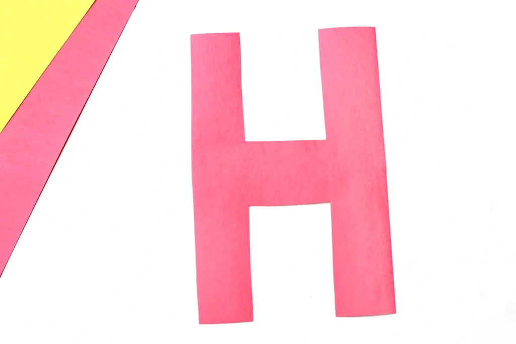 Letter H House Craft - Cultivating Brilliant Minds Part of a bold red letter H on a white background with a yellow diagonal stripe along the left edge.