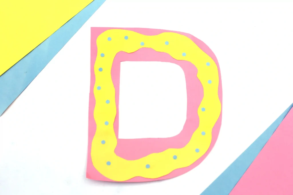 Letter D Craft - Cultivating Brilliant Minds a letter d craft that has a pink letter d with yellow squiggly frosting on top made from yellow construction paper, and blue circles for sprinkles
