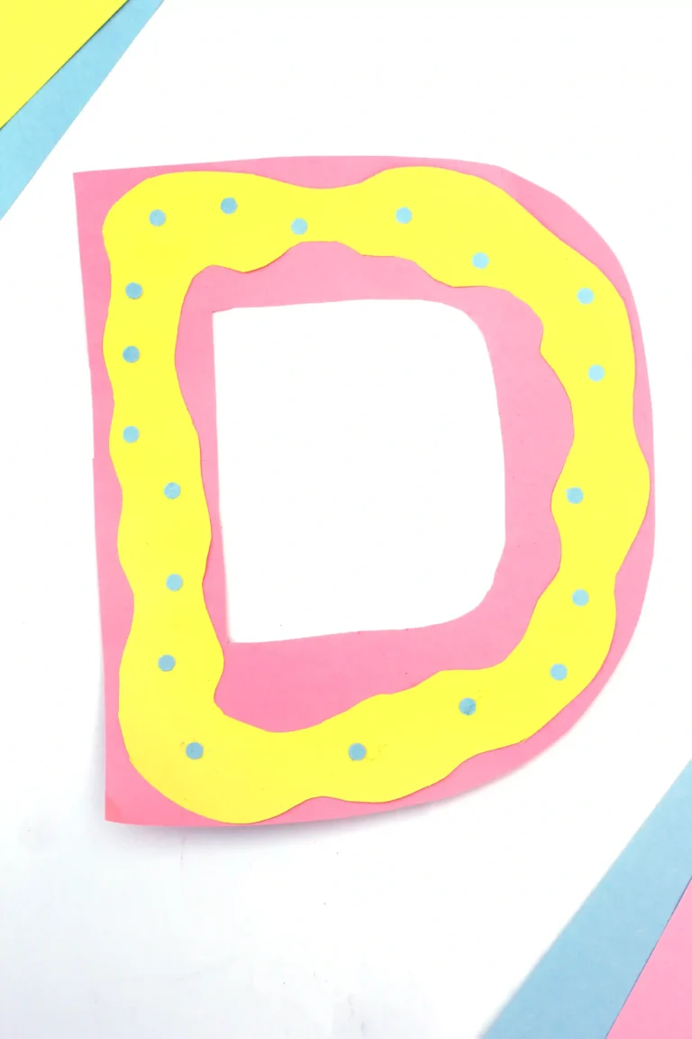 a letter d craft that has a pink letter d with yellow squiggly frosting on top made from yellow construction paper, and blue circles for sprinkles