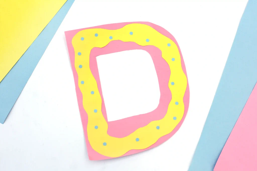 Letter D Craft - Cultivating Brilliant Minds a letter d craft that has a pink letter d with yellow squiggly frosting on top made from yellow construction paper, and blue circles for sprinkles