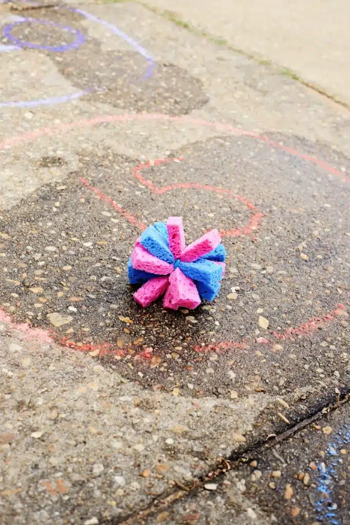 DIY Sponge Toss - Cultivating Brilliant Minds Colorful pink and blue star-shaped sponge on a concrete sidewalk near chalk drawings.