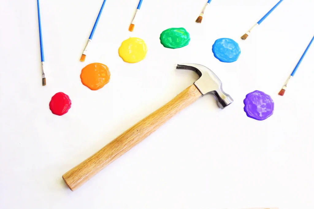 Hammer Father's Day Activity - Cultivating Brilliant Minds colorful paint blobs with brushes scattered around and a hammer on a white surface.