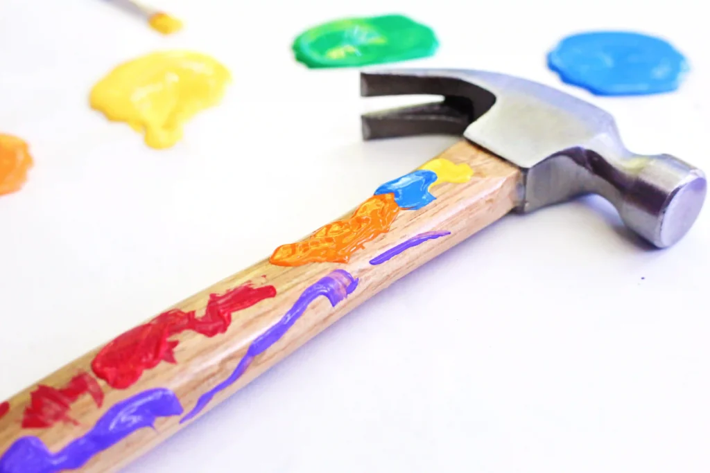 Hammer Father's Day Activity - Cultivating Brilliant Minds a father's day activity - Close-up of a hammer with colorful paint on the handle; bright paint blobs in the blurred background.