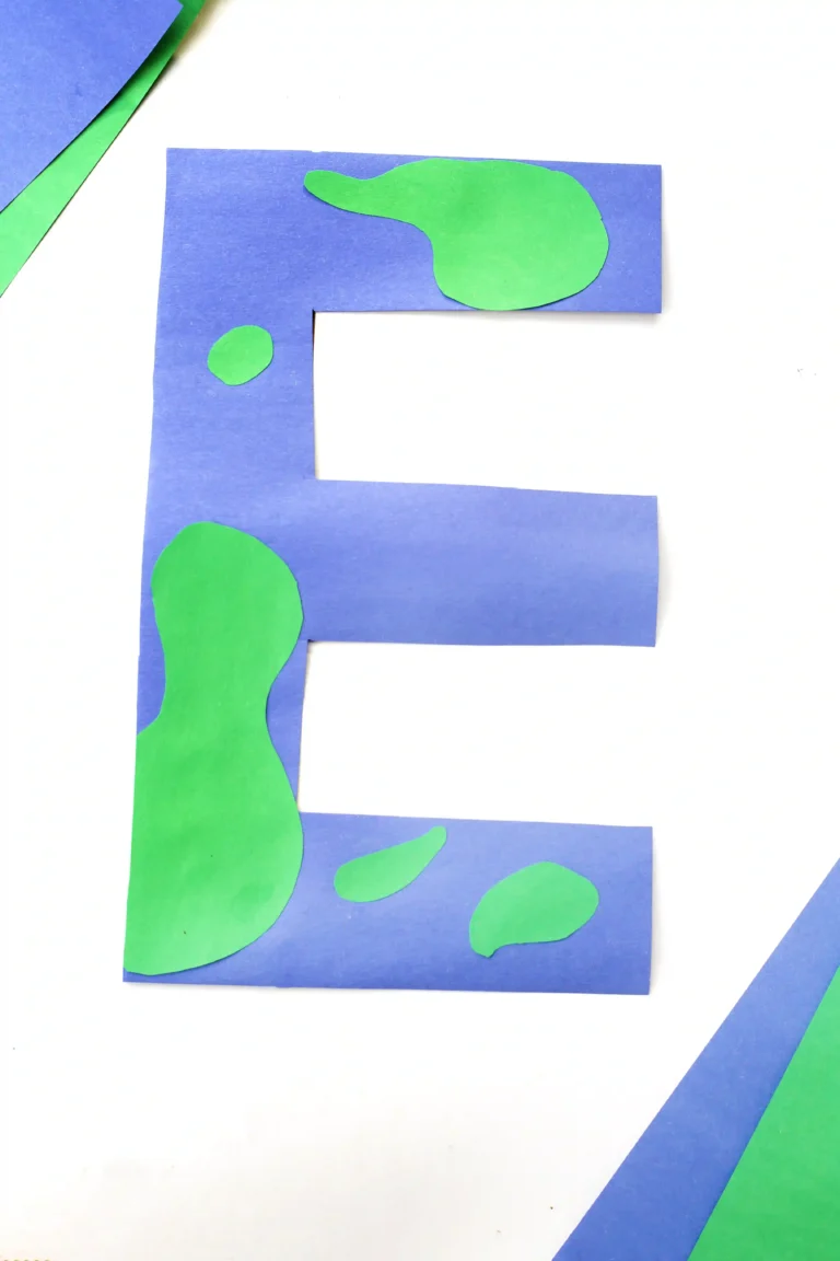 Blue paper cutout in the shape of the letter E with green irregular patches on a white background, in a collage art style.