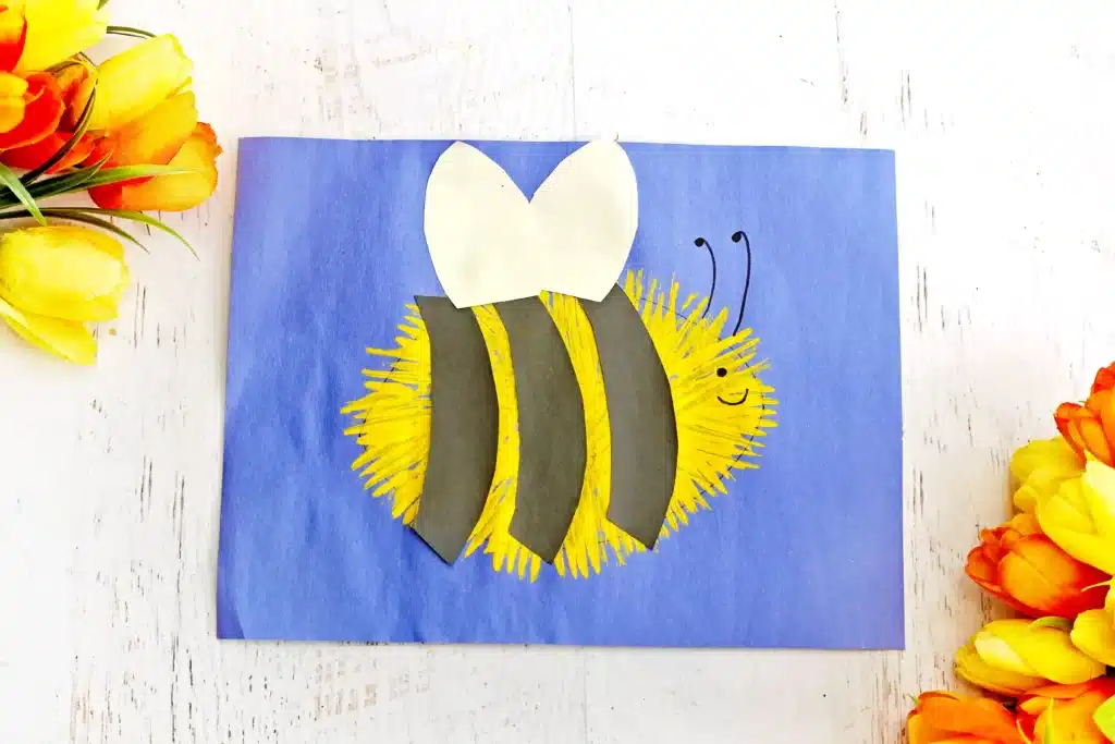 Fork Painted Bee - Cultivating Brilliant Minds Craft bee on blue card: yellow fluffy body with black stripes and white heart wings, smiling face.