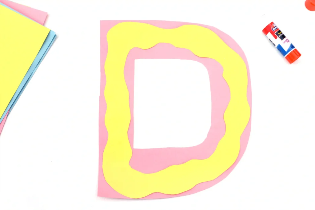 Letter D Craft - Cultivating Brilliant Minds letter d cut out of pink construction paper with yellow construction paper squiggly "frosting" on top