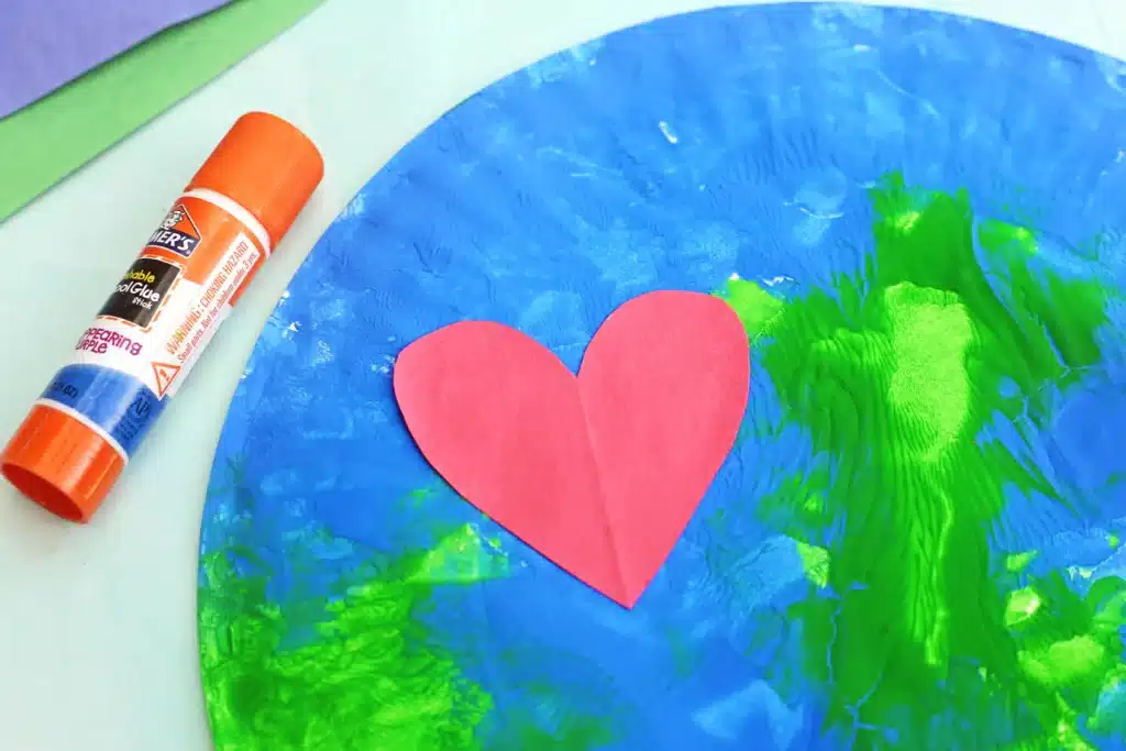 No-Mess Earth Day Painting - Cultivating Brilliant Minds a paper plate painted with green and blue paint to look like an Earth with a red construction paper heart
