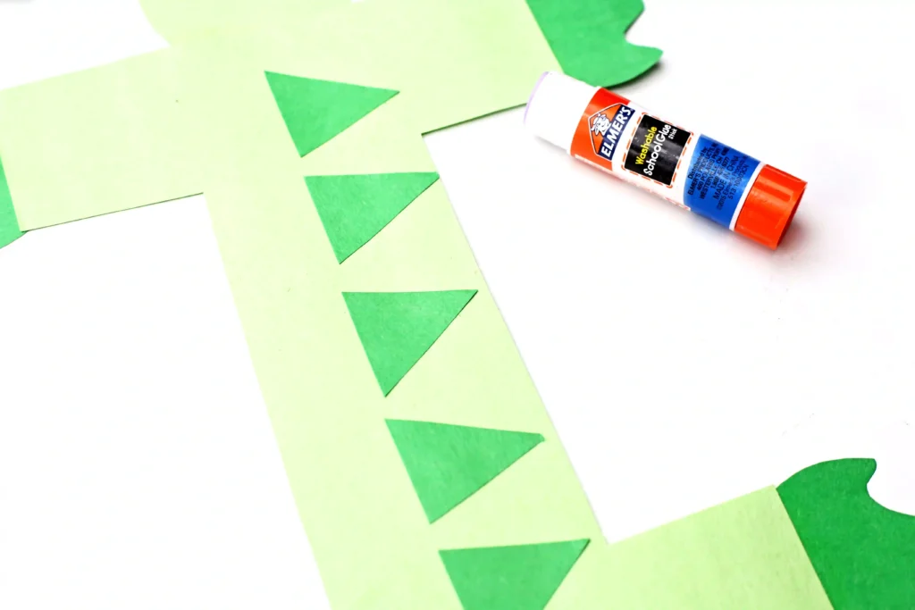 Letter I Iguana Craft - Cultivating Brilliant Minds Glue stick beside lime green construction paper with green triangular shapes cut out.