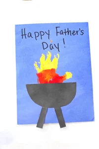 a yellow, orange, and red handprint with a construction paper grill on blue paper that reads" happy father's day!"