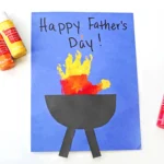 a yellow, orange, and red handprint with a construction paper grill on blue paper that reads" happy father's day!"