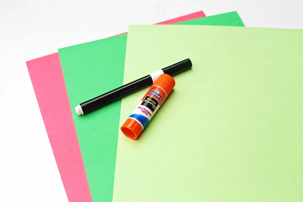 Letter I Iguana Craft - Cultivating Brilliant Minds Glue stick placed on overlapping pink, green, and lime construction paper for crafts, ready for a DIY project.