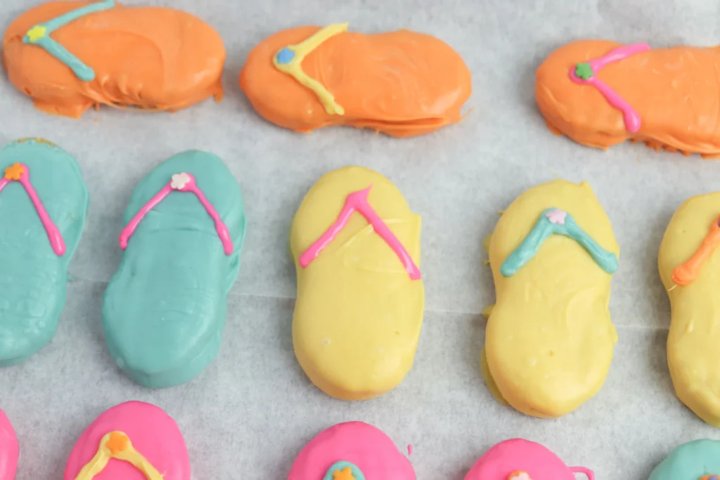 Flip Flop Cookies - Cultivating Brilliant Minds Row of pastel-frosted nutter butter cookies with colorful melted chocolate designs on a baking sheet made to look like flip flops