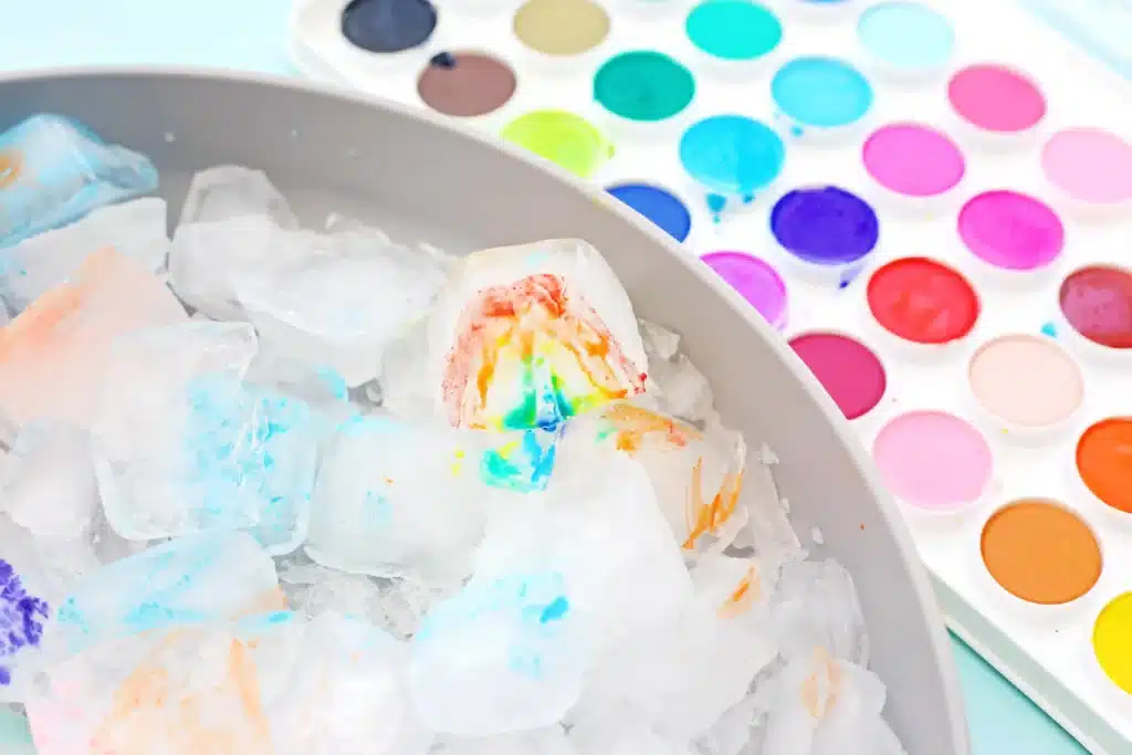 Ice Painting - Cultivating Brilliant Minds Colorful ice cubes in a bowl, with a rainbow paint palette in the background.