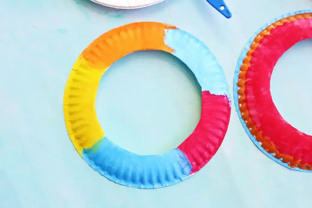 Paper Plate Ring Toss Game - Cultivating Brilliant Minds Colorful paper plate wreaths painted in rainbow segments on a light blue surface
