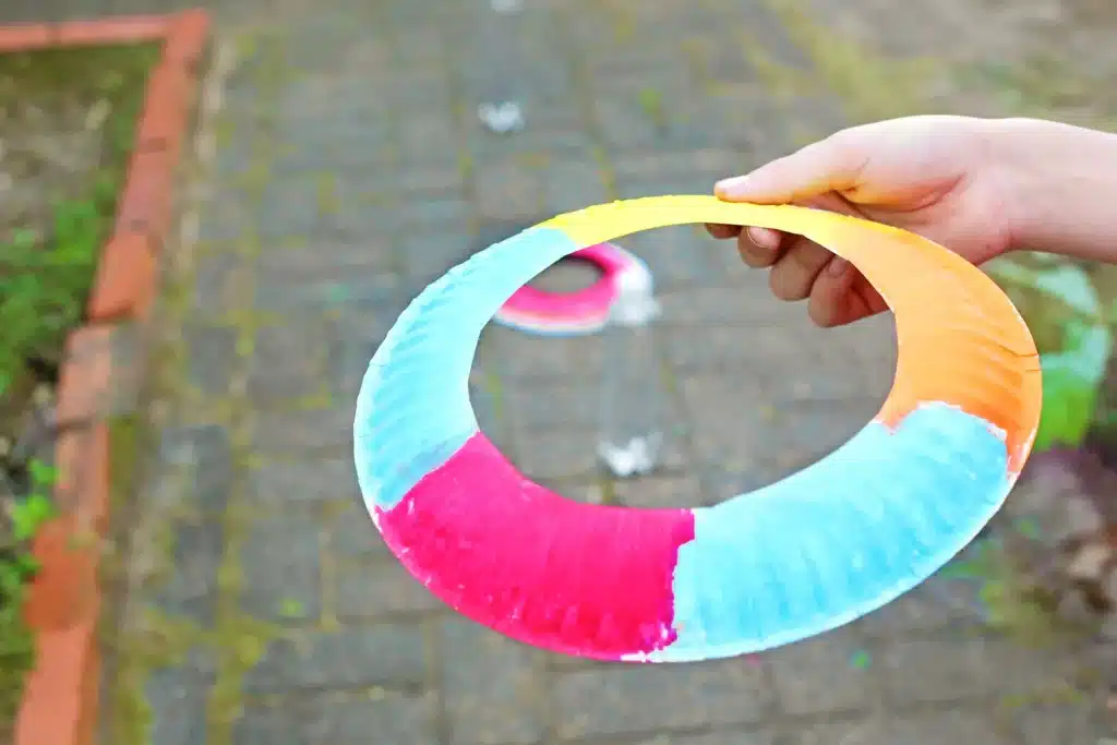 Paper Plate Ring Toss Game - Cultivating Brilliant Minds a person holding a paper plate frisbee with the middle cut out