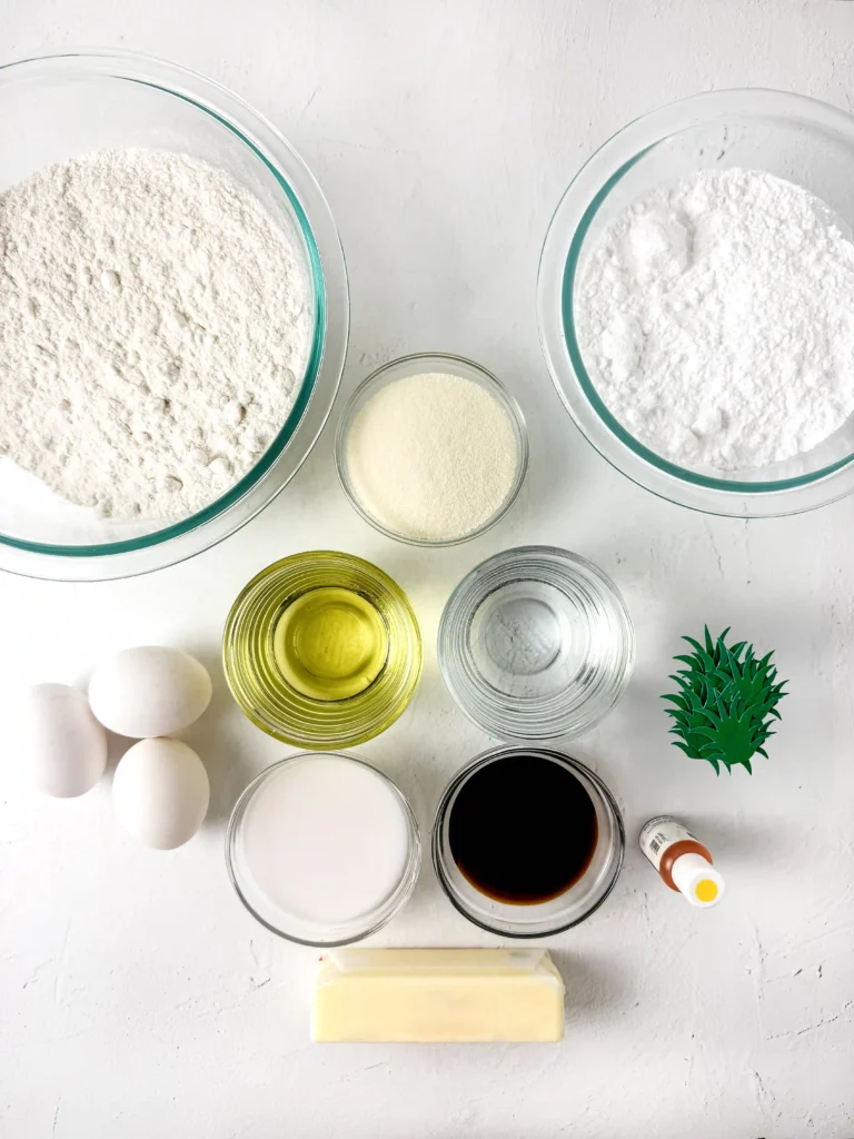 Pineapple Cupcakes - Cultivating Brilliant Minds Top-down view of baking ingredients: bowls of flour, eggs, butter, oil, sugar, and vanilla on a white surface.