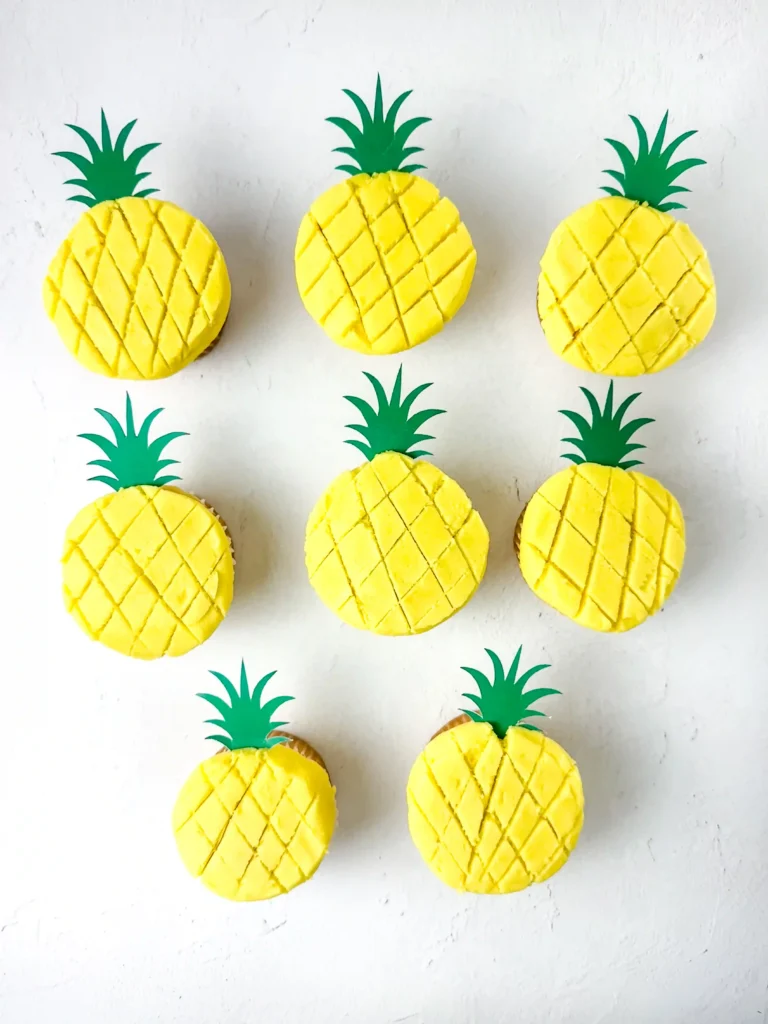 Pineapple Cupcakes - Cultivating Brilliant Minds Row of yellow pineapple-shaped cupcakes with green leaf toppers on a white surface.