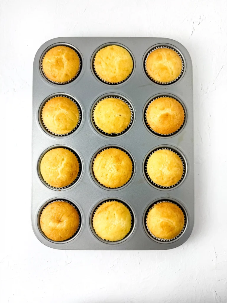 Pineapple Cupcakes - Cultivating Brilliant Minds Top-down view of a muffin pan with twelve golden cupcakes in paper liners on a white surface.