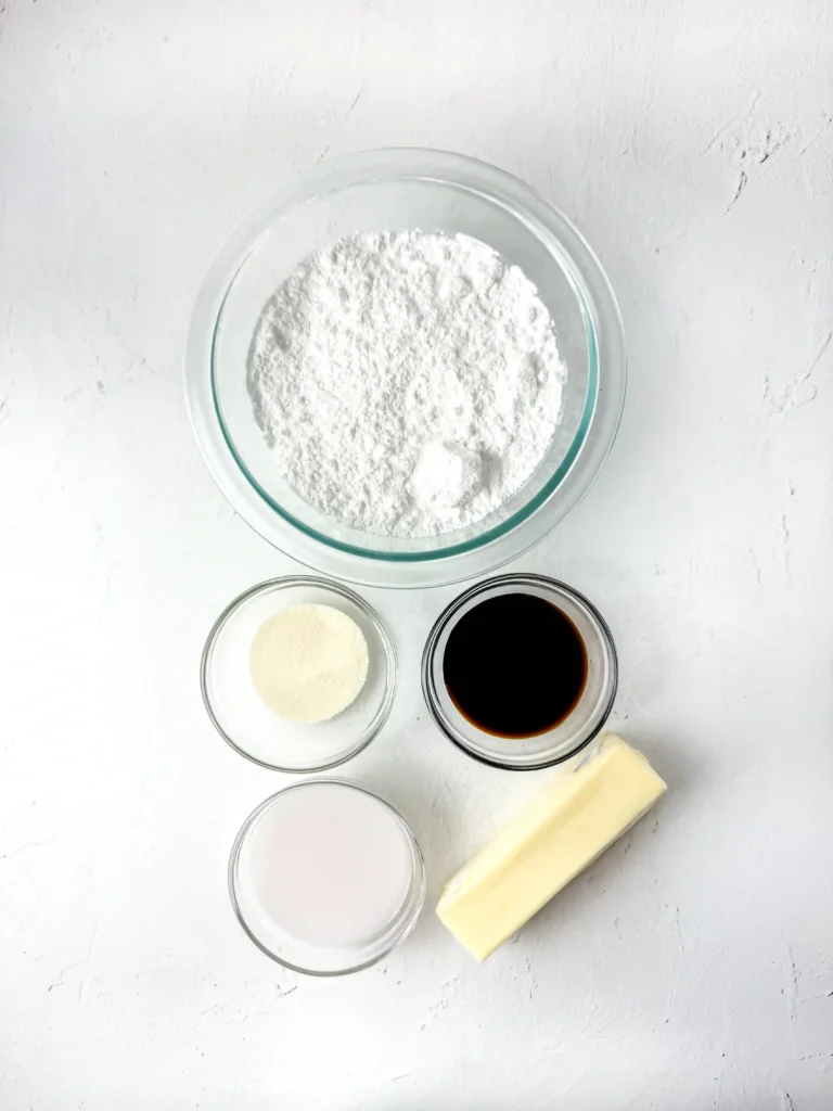 Pineapple Cupcakes - Cultivating Brilliant Minds Top-down view of baking ingredients: flour in a glass bowl, sugar, vanilla extract, milk, and a stick of butter on a white surface