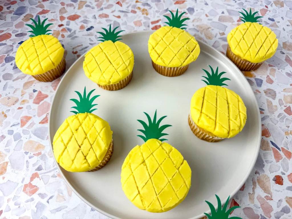 Pineapple Cupcakes - Cultivating Brilliant Minds Yellow cupcakes decorated to look like pineapples with green paper toppers on a white plate.